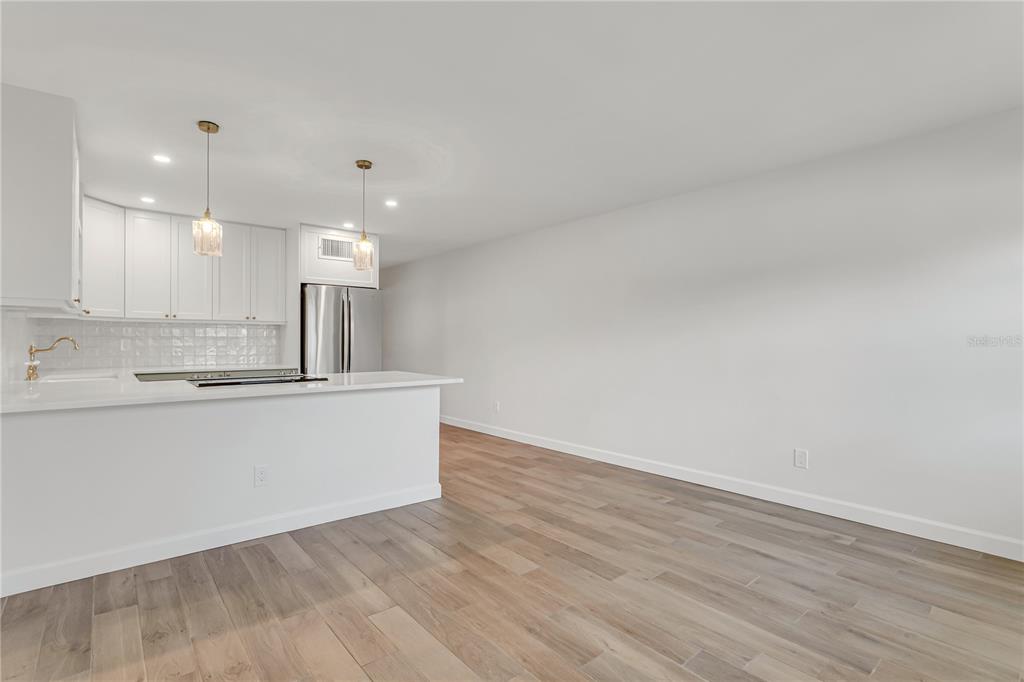 A modern kitchen with white cabinets and a breakfast bar opens into a living area — 216 36TH AVENUE N UNIT 202B, ST PETERSBURG, FL