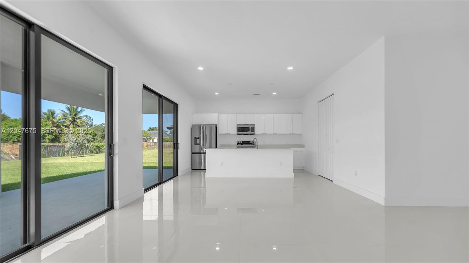 A modern kitchen with white cabinetry and an island overlooks a backyard through sliding doors — 23120 SW 154 CT, Miami FL 33170, MIAMI, FL