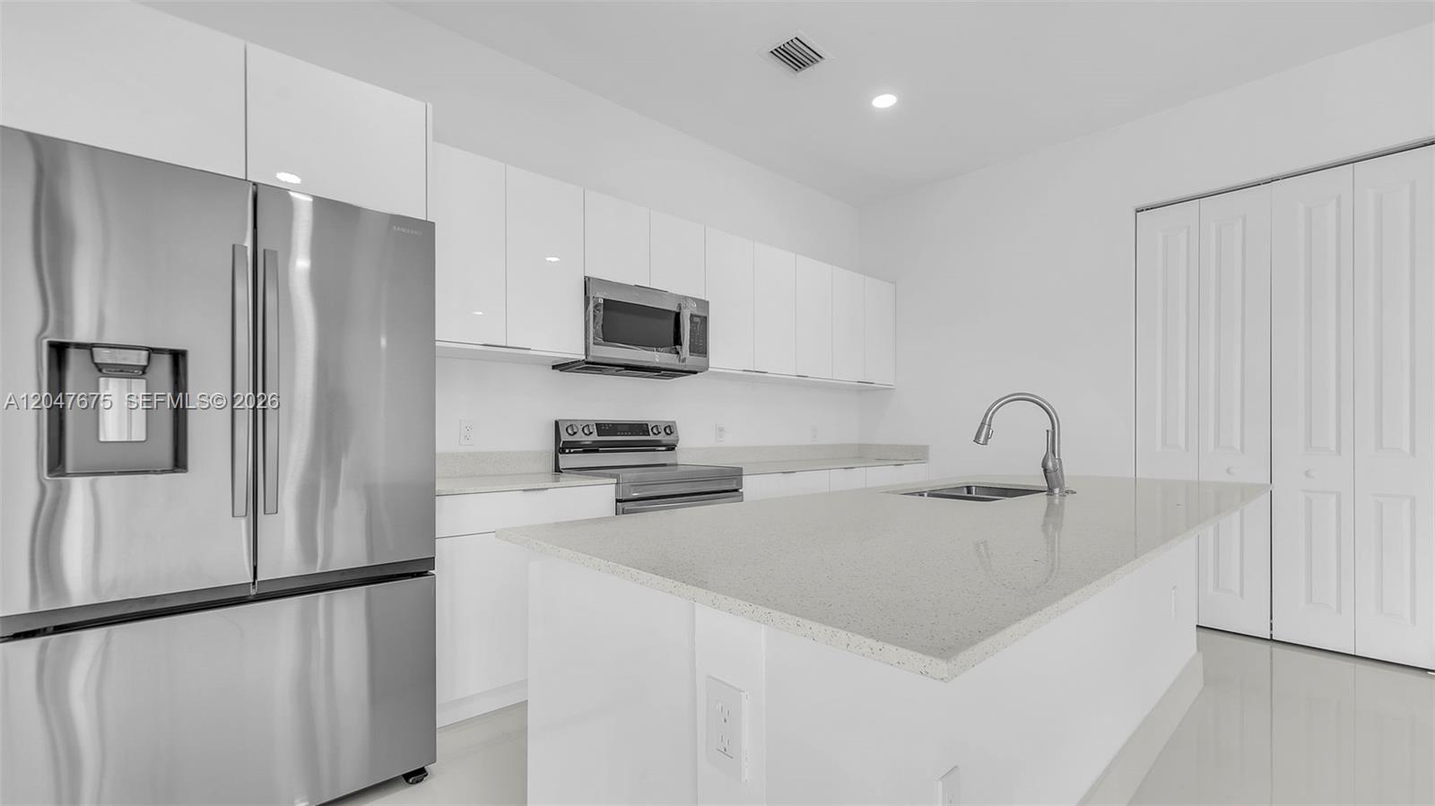 A modern kitchen features white cabinetry, stainless steel appliances, and a quartz-topped island — 23120 SW 154 CT, Miami FL 33170, MIAMI, FL