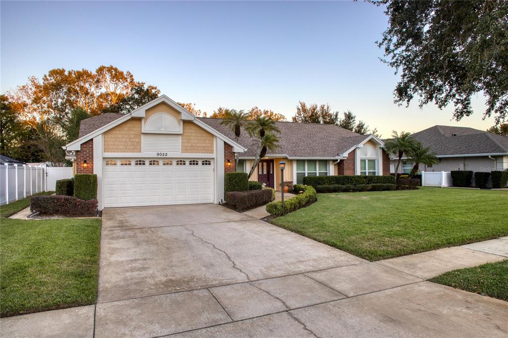 A single-story house with a two-car garage, tan siding, and a manicured front lawn — 9052 PALOS VERDE DRIVE, ORLANDO, FL