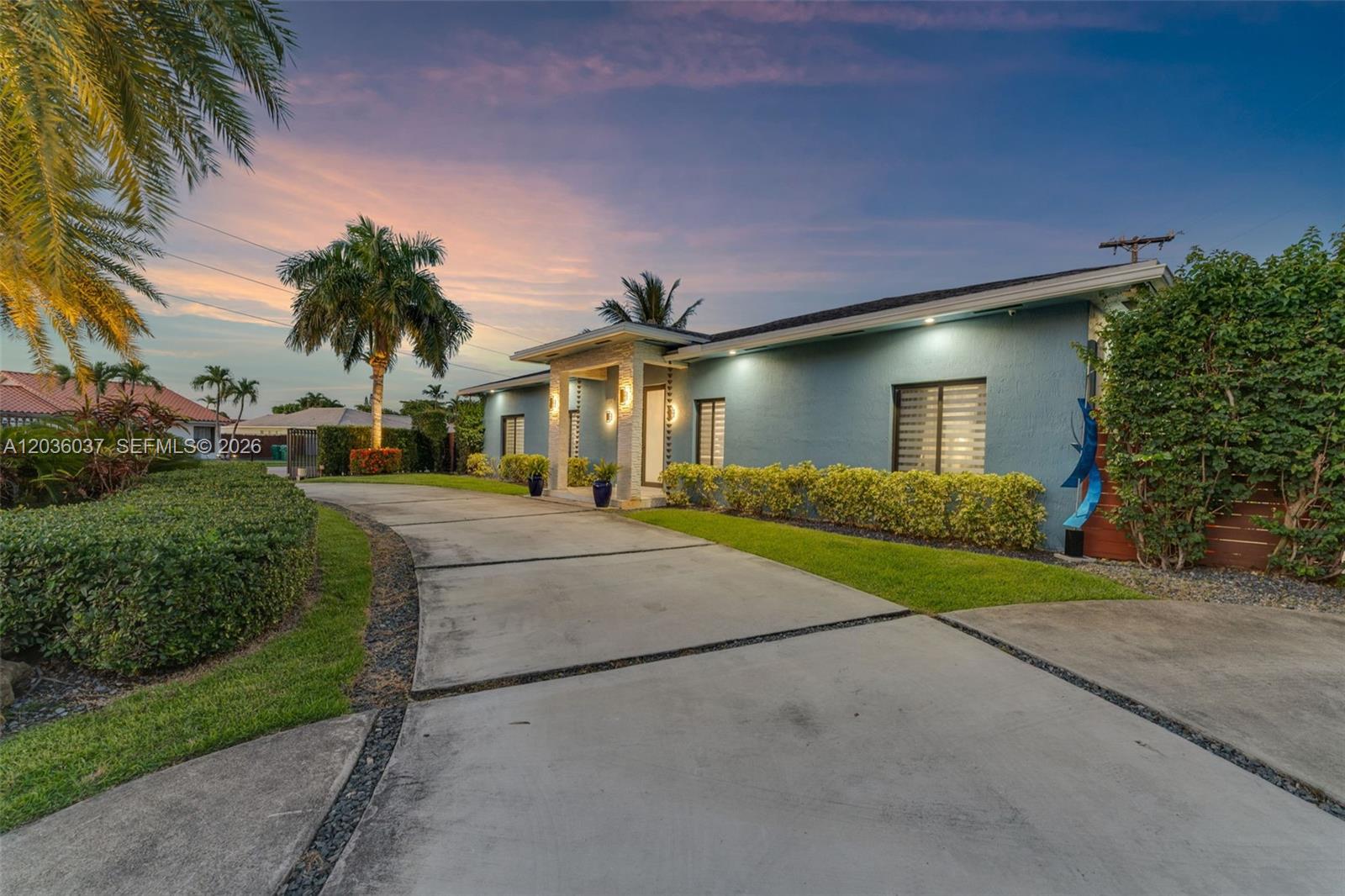 A blue single-story house features a concrete driveway and a covered entryway at sunset — 1201 SW 92nd Ave, Miami FL 33174, MIAMI, FL