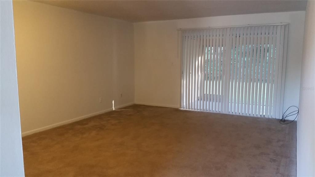 An empty room features beige wall-to-wall carpeting, white walls, and a large sliding glass door — 7312 BALBOA DRIVE UNIT 7312, ORLANDO, FL