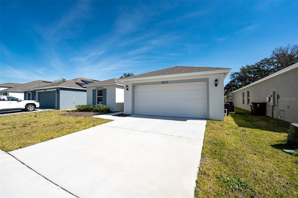 A single-story house exterior features a white garage door, a concrete driveway, and light-colored siding — 3473 YARIAN DRIVE, HAINES CITY, FL