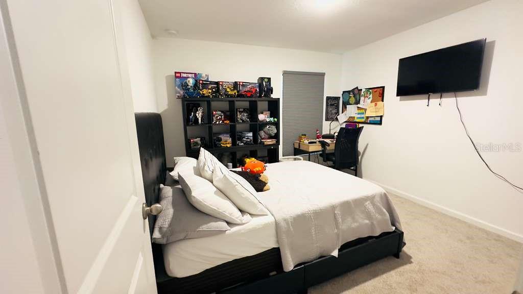 A bedroom features a black bed frame, a storage shelving unit, and a wall-mounted television — 3473 YARIAN DRIVE, HAINES CITY, FL