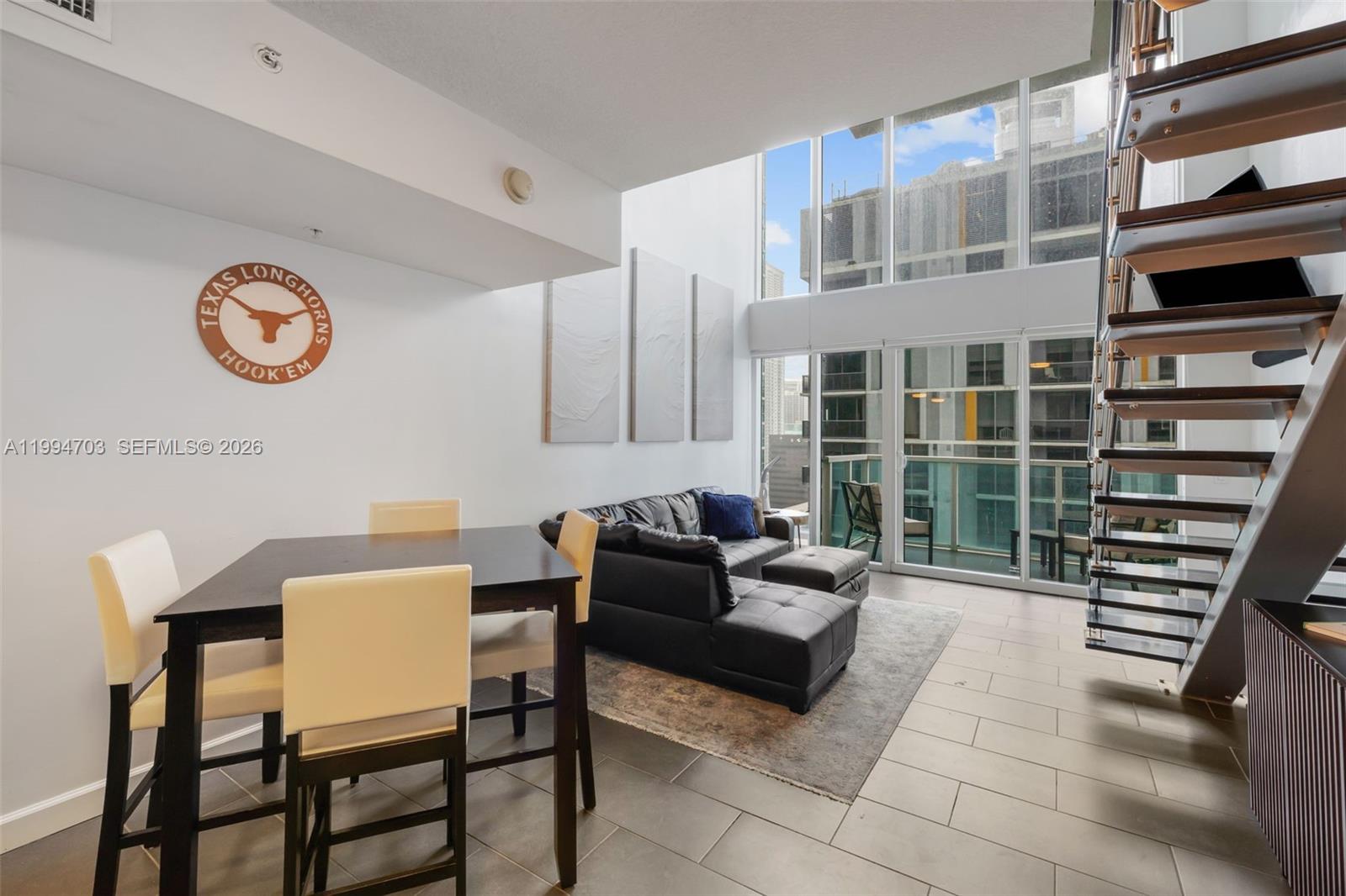 A modern living and dining area features a staircase, floor-to-ceiling windows, and tile flooring — 41 SE 5th St # 1306, Miami FL 33131, MIAMI, FL