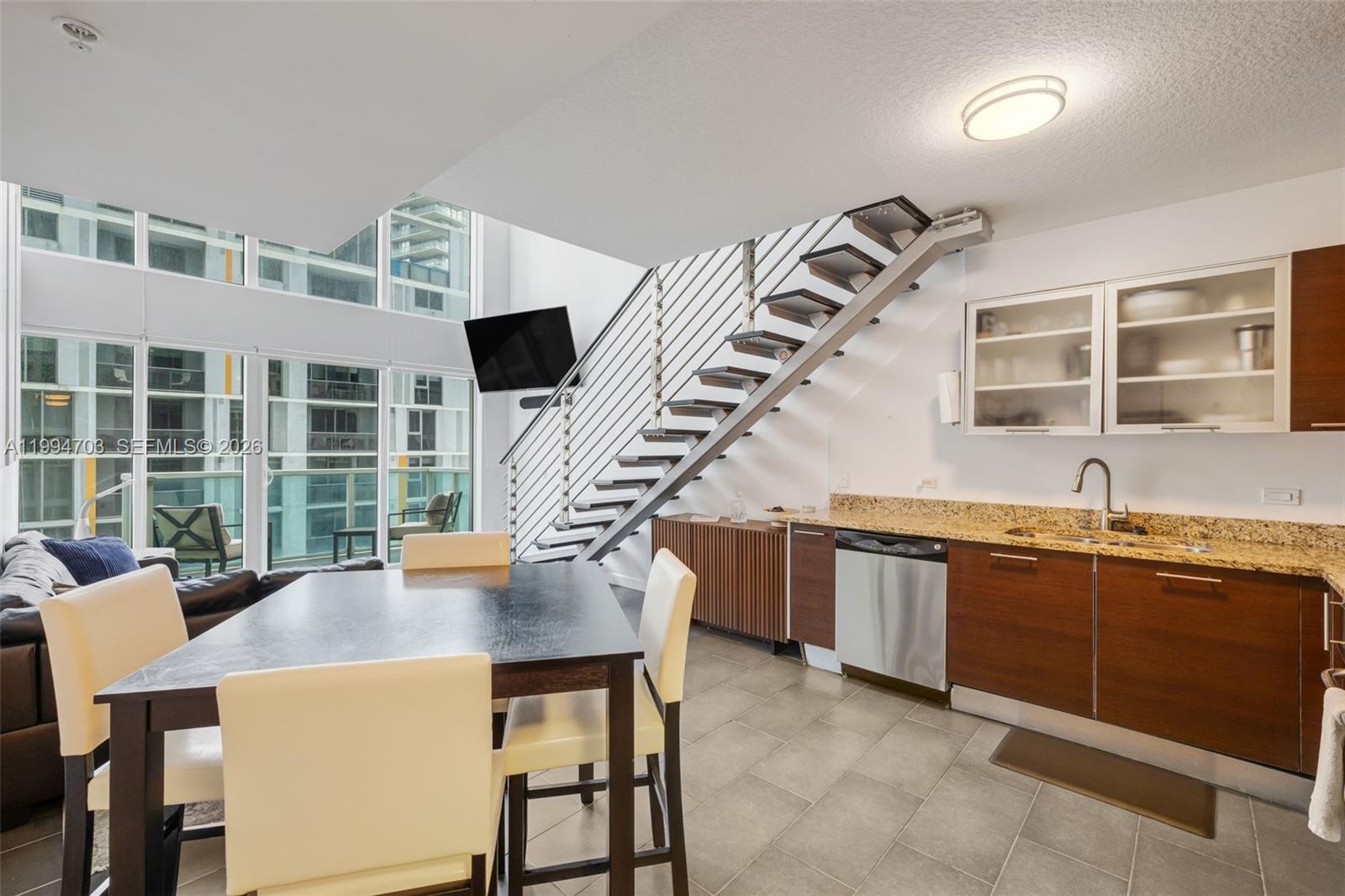 A modern kitchen and dining area feature a floating staircase, tile floors, and floor-to-ceiling windows — 41 SE 5th St # 1306, Miami FL 33131, MIAMI, FL