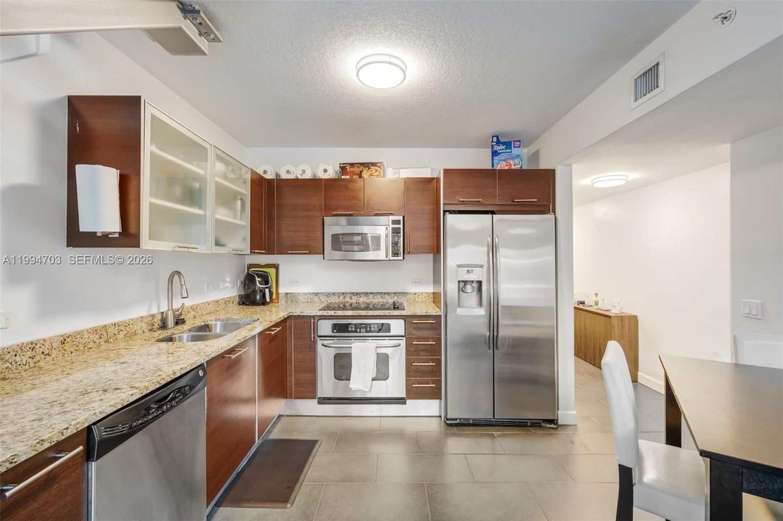 A kitchen features wood cabinets, granite countertops, stainless steel appliances, and large floor tiles — 41 SE 5th St # 1306, Miami FL 33131, MIAMI, FL