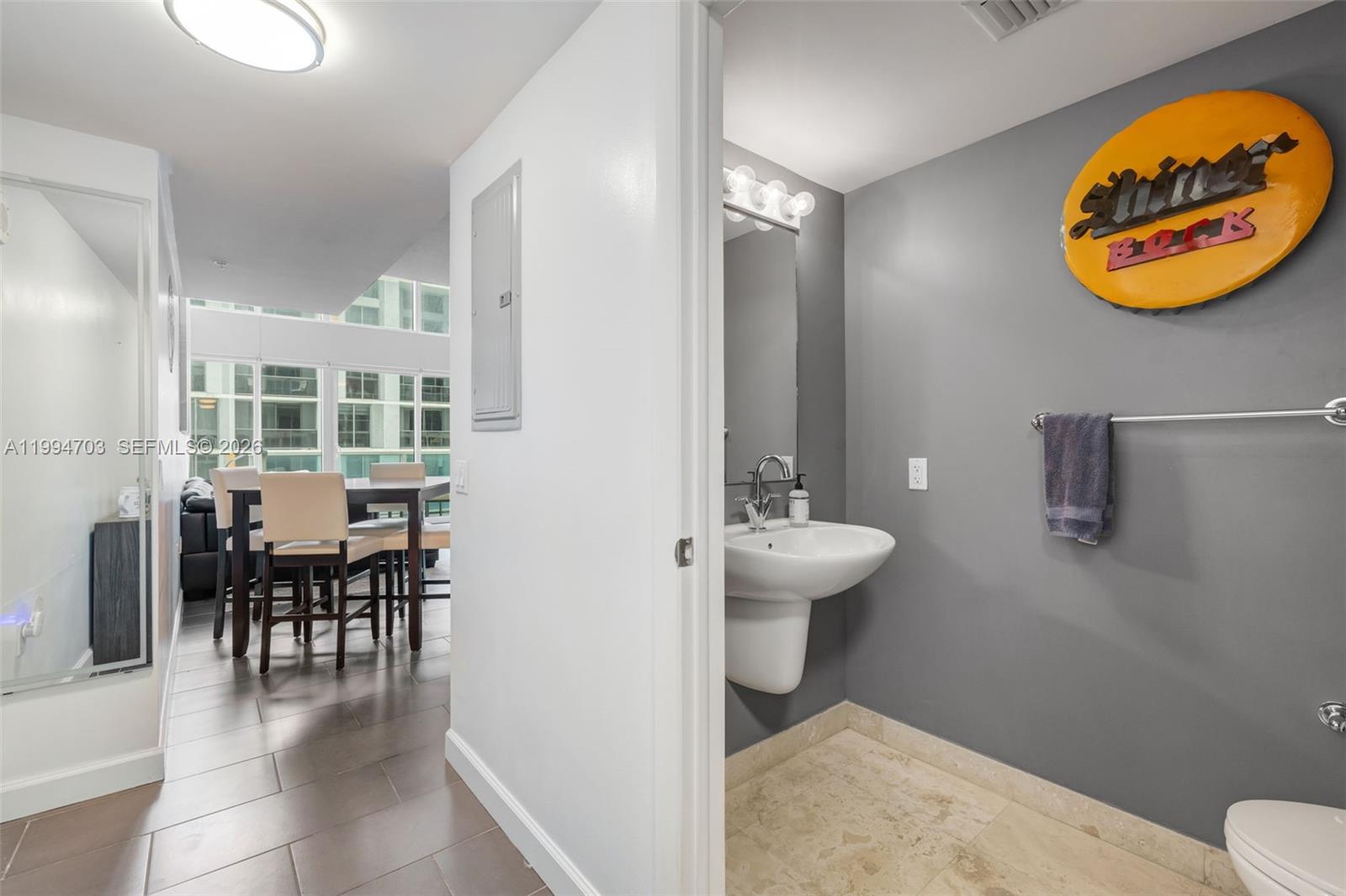A small bathroom with a pedestal sink and gray walls sits beside a dining area — 41 SE 5th St # 1306, Miami FL 33131, MIAMI, FL
