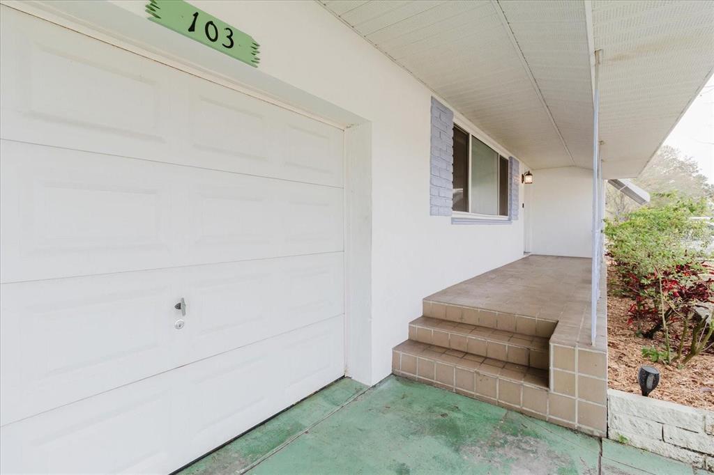 A white garage door sits beside a tiled porch with steps leading to a front entrance — 103 N METEOR AVENUE, CLEARWATER, FL