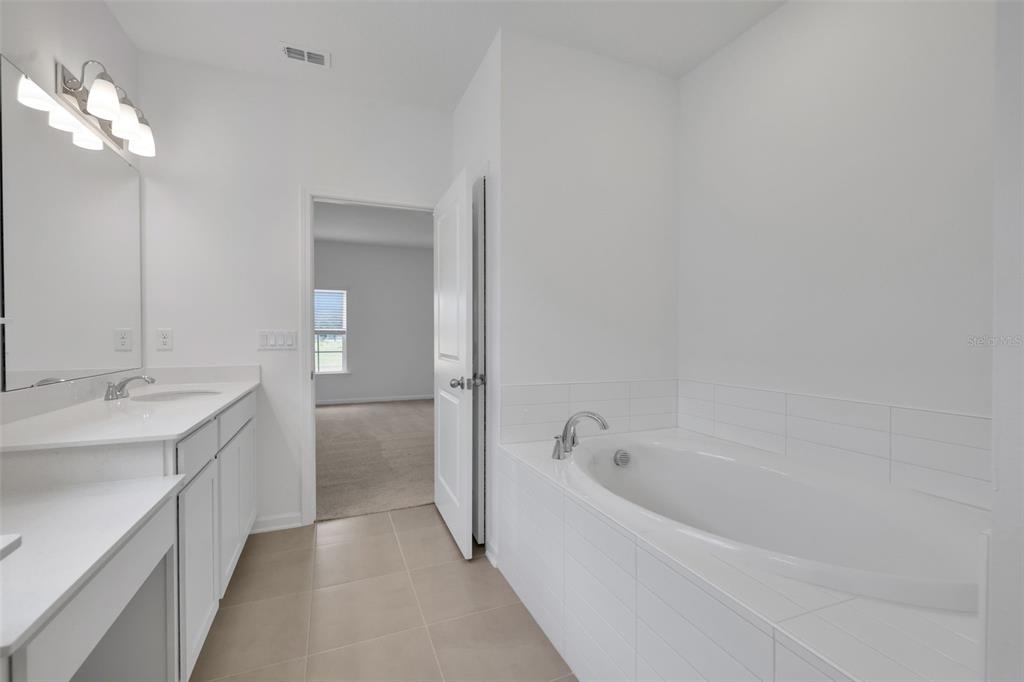 A bright bathroom features a white vanity, a soaking tub, and tile flooring — 3906 HOLSTEIN WAY, GREEN COVE SPRINGS, FL