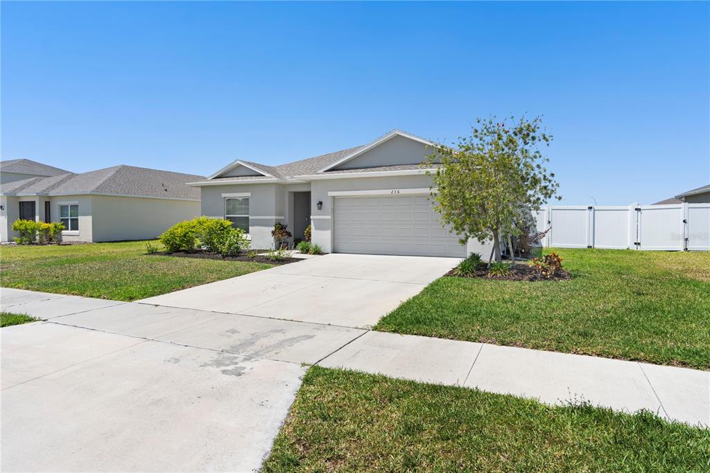 A single-story suburban house with a gray exterior, two-car garage, and a white vinyl fence — 236 AQUAMARINE LANE, KISSIMMEE, FL