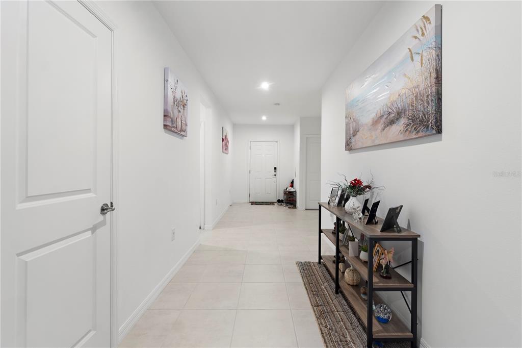 A bright hallway features white walls, tiled flooring, a console table, and wall art — 236 AQUAMARINE LANE, KISSIMMEE, FL