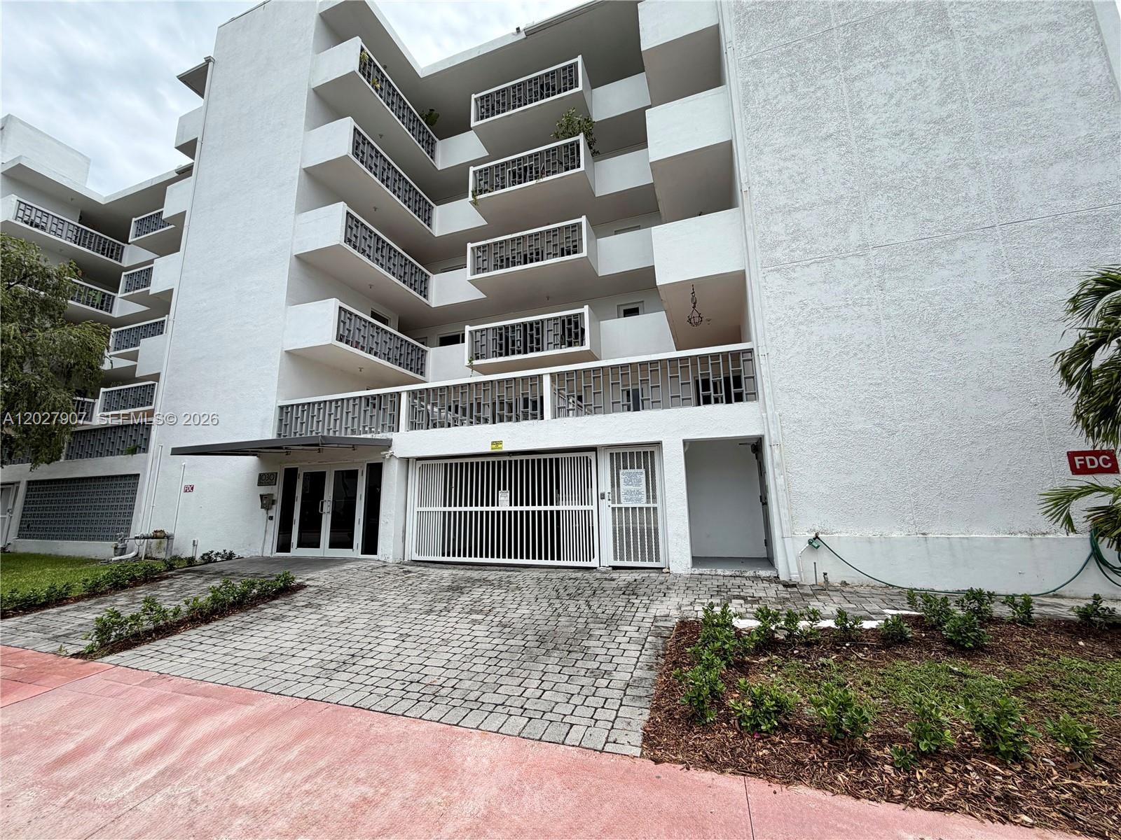 The exterior of a multi-story white apartment building features balconies and a gated garage entrance — 1030 9th St # 204, Miami Beach FL 33139, MIAMI BEACH, FL