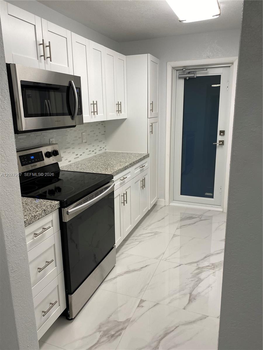 A galley kitchen features white cabinets, stainless steel appliances, granite countertops, and light marble flooring — 1030 9th St # 204, Miami Beach FL 33139, MIAMI BEACH, FL