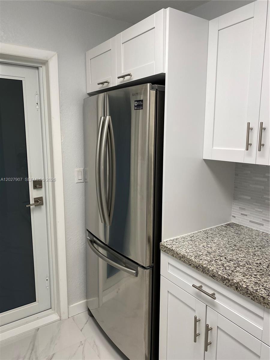 A stainless steel refrigerator is positioned between white kitchen cabinets and a glass-paneled door — 1030 9th St # 204, Miami Beach FL 33139, MIAMI BEACH, FL