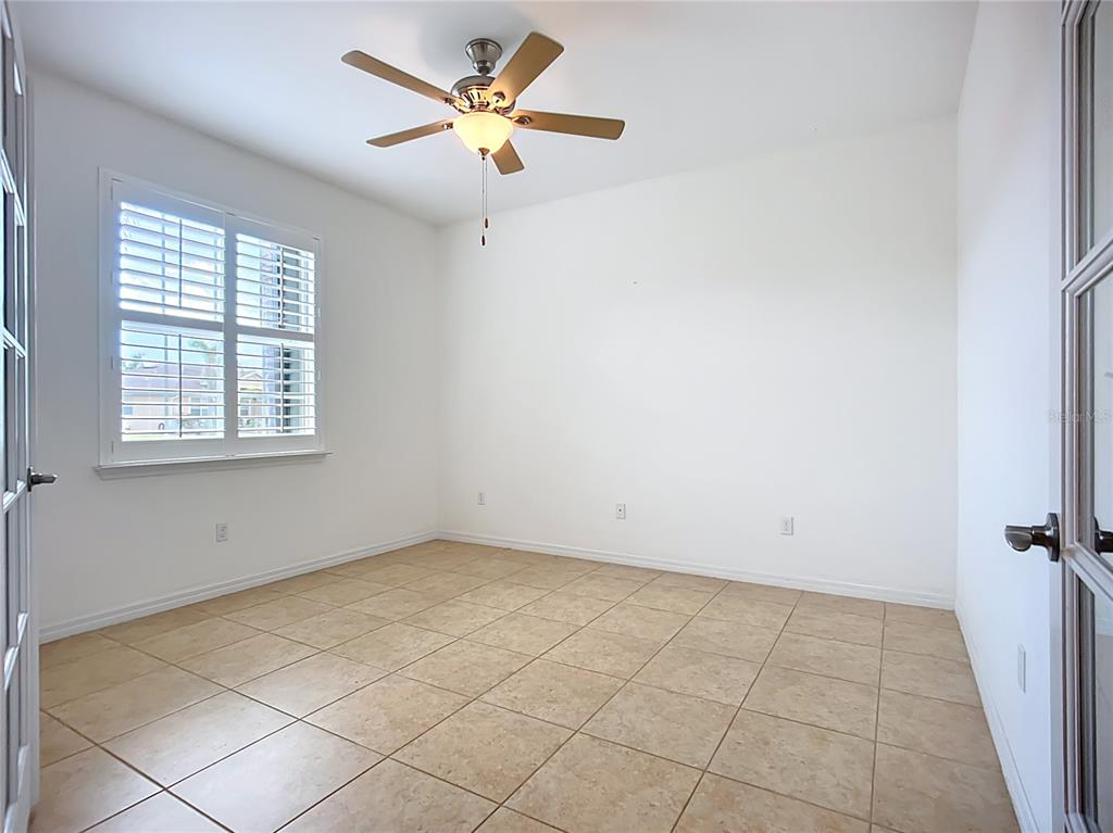 An empty room with white walls, tile flooring, a ceiling fan, and a shuttered window — 5384 LAYTON DRIVE, VENICE, FL