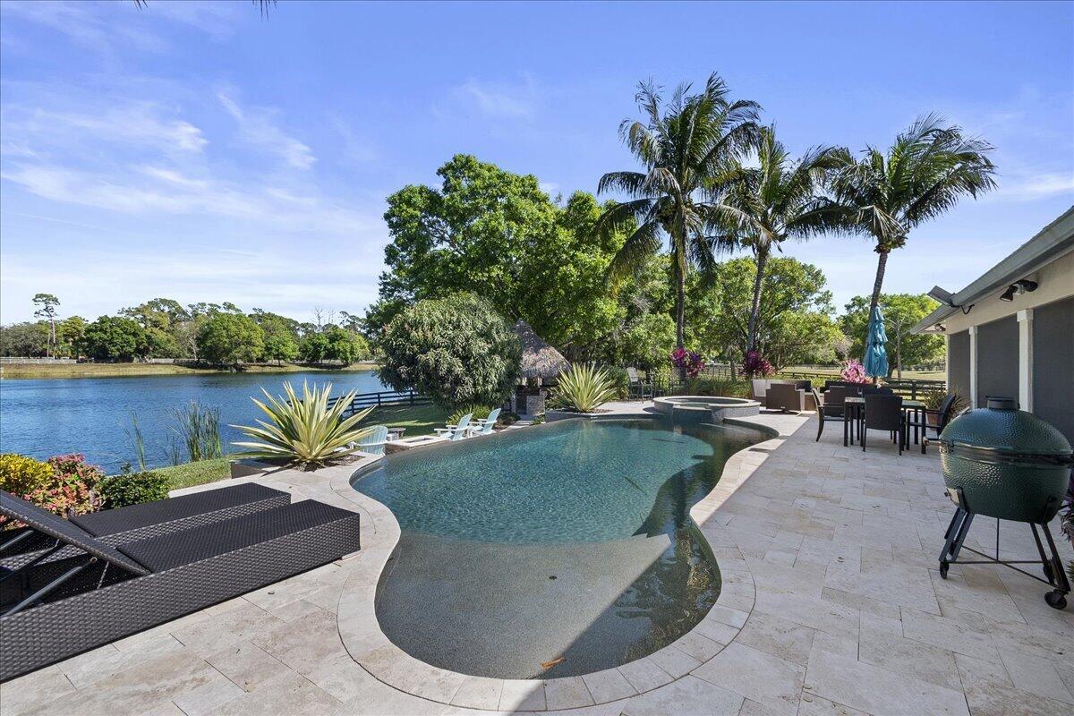 A backyard patio features a freeform swimming pool, a hot tub, and a lake view — 10975 Randolph Siding Road, Jupiter FL 33478, JUPITER, FL