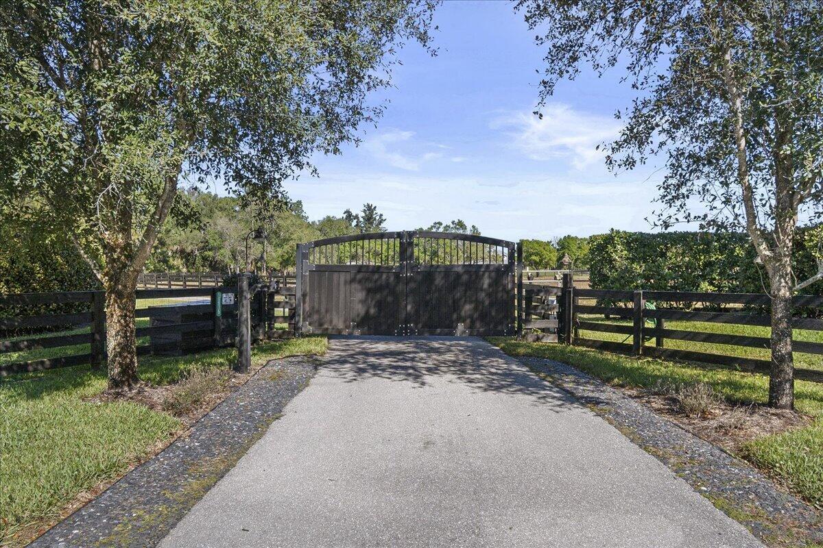 A paved driveway leads to a closed dark wooden gate flanked by black wooden fencing — 10975 Randolph Siding Road, Jupiter FL 33478, JUPITER, FL