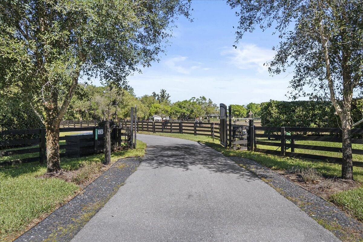 A paved driveway leads through an open gate into a fenced property with mature trees — 10975 Randolph Siding Road, Jupiter FL 33478, JUPITER, FL