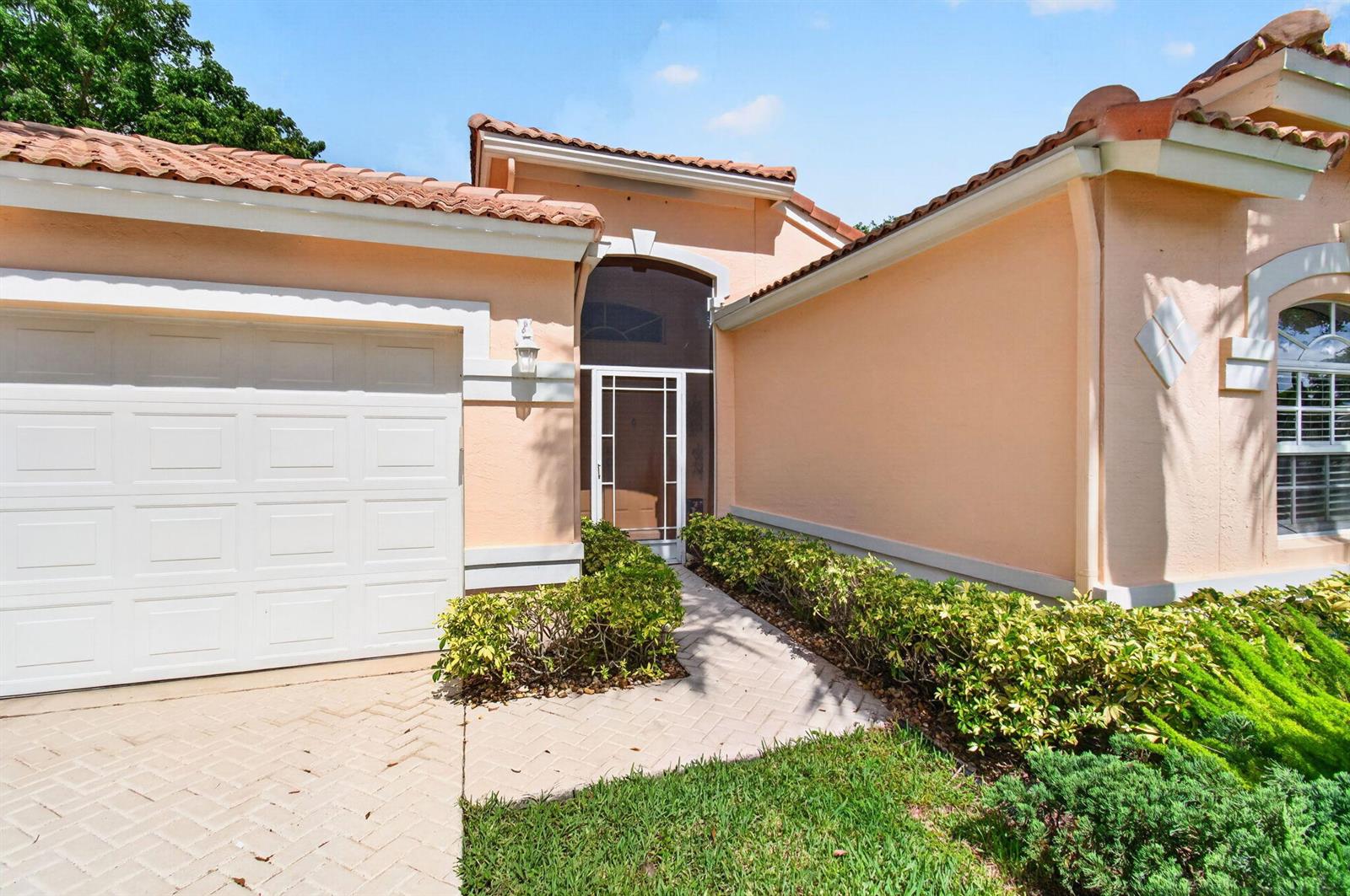 A peach-colored house exterior features a white garage door, a tiled roof, and a walkway — 6265 Coral Reef Terrace, Boynton Beach FL 33437, BOYNTON BEACH, FL