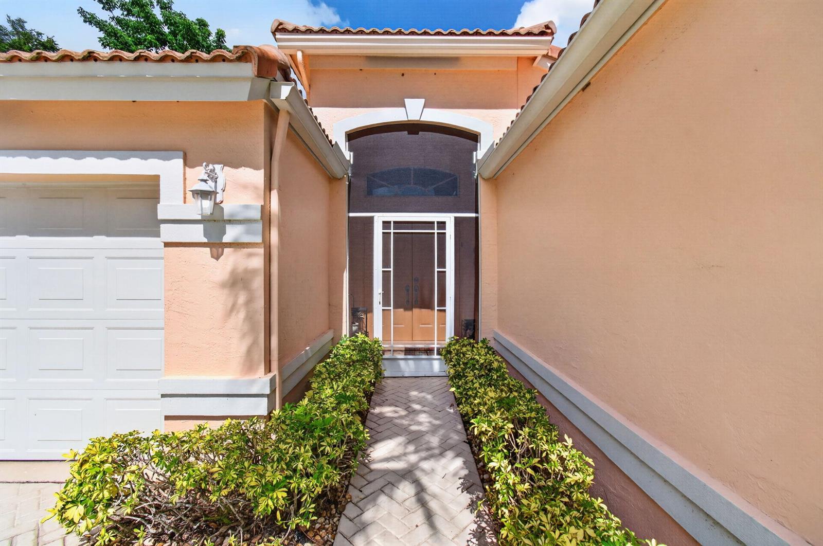 A peach-colored house exterior features a front walkway lined with shrubs leading to the entrance — 6265 Coral Reef Terrace, Boynton Beach FL 33437, BOYNTON BEACH, FL