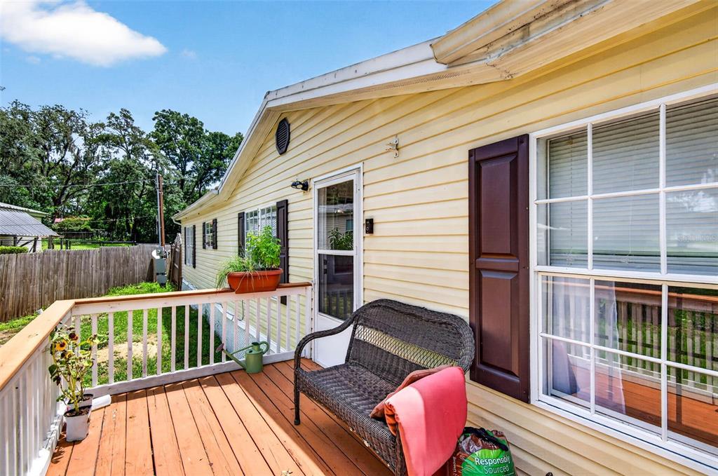 A wooden deck with a wicker bench sits outside a yellow house with white trim — 12641 IDLEWOOD DRIVE, THONOTOSASSA, FL