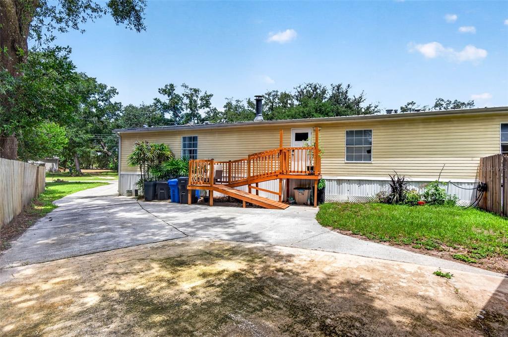 The exterior of a single-story home features yellow siding, a wooden deck with a ramp, and a concrete driveway — 12641 IDLEWOOD DRIVE, THONOTOSASSA, FL