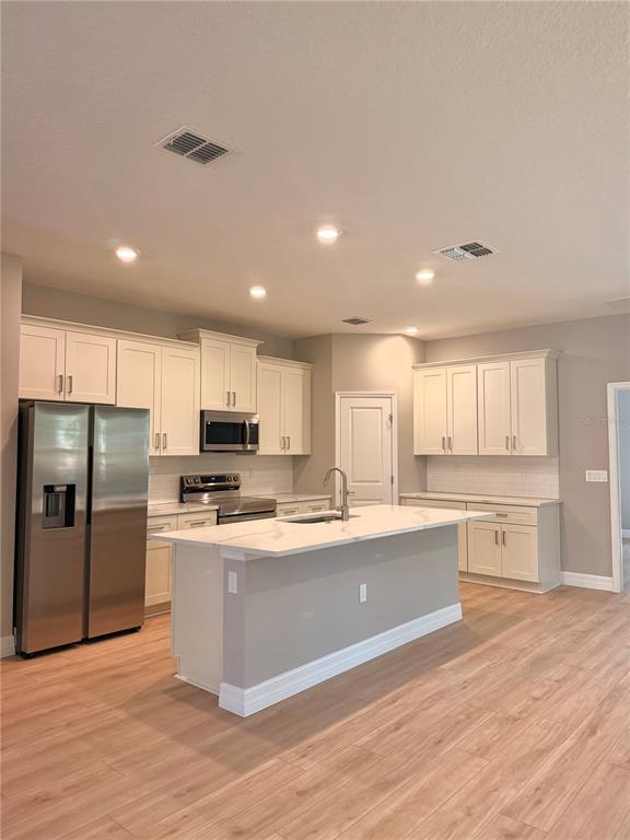 A kitchen features white cabinets, stainless steel appliances, a center island, and light wood flooring — 5226 E PRENTICE LANE, INVERNESS, FL