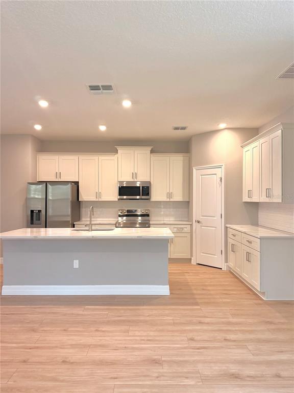 A modern kitchen features white cabinetry, stainless steel appliances, a center island, and wood-look flooring — 5226 E PRENTICE LANE, INVERNESS, FL