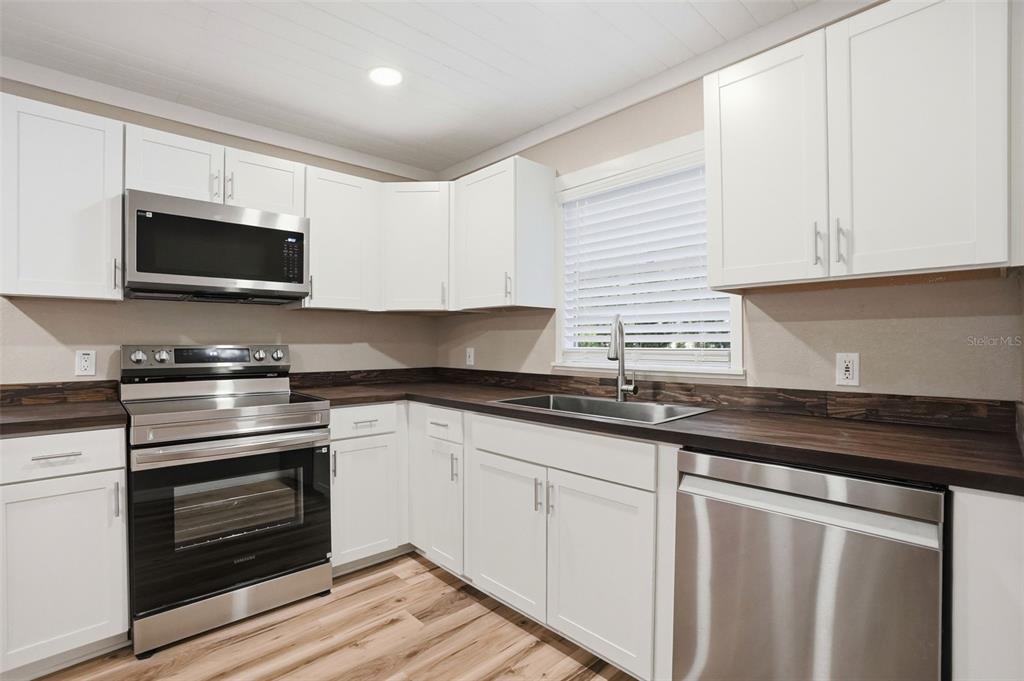 A kitchen features white cabinets, dark wood countertops, stainless steel appliances, and light wood flooring — 65 MARKHAM LANE, BROOKSVILLE, FL