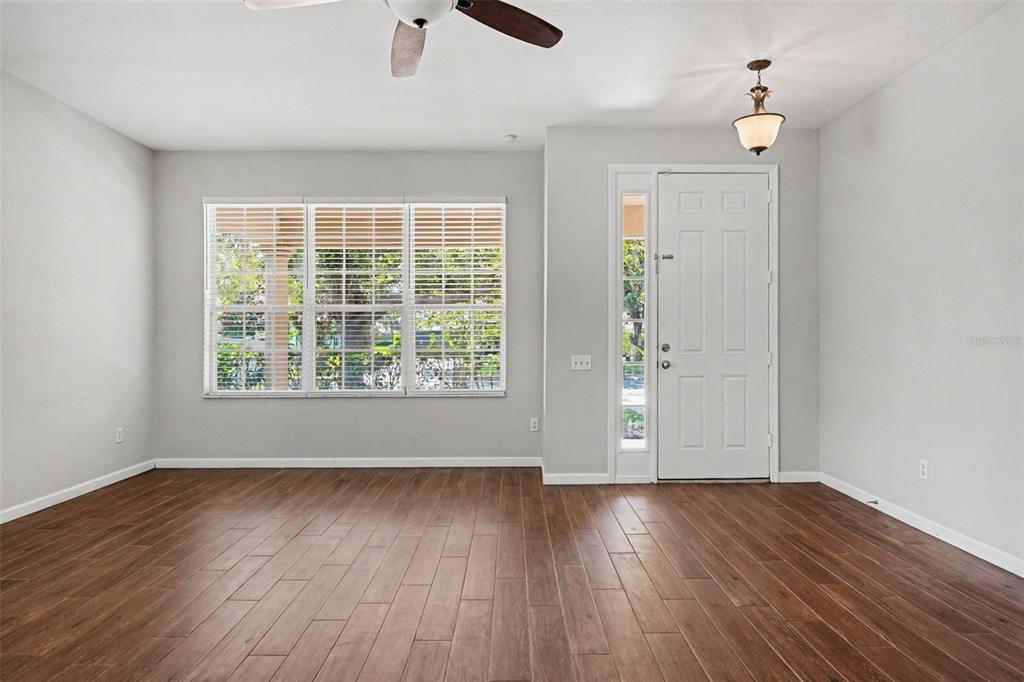 An empty room features wood-look flooring, a ceiling fan, a front door, and large windows — 2210 GRANGER AVENUE, KISSIMMEE, FL