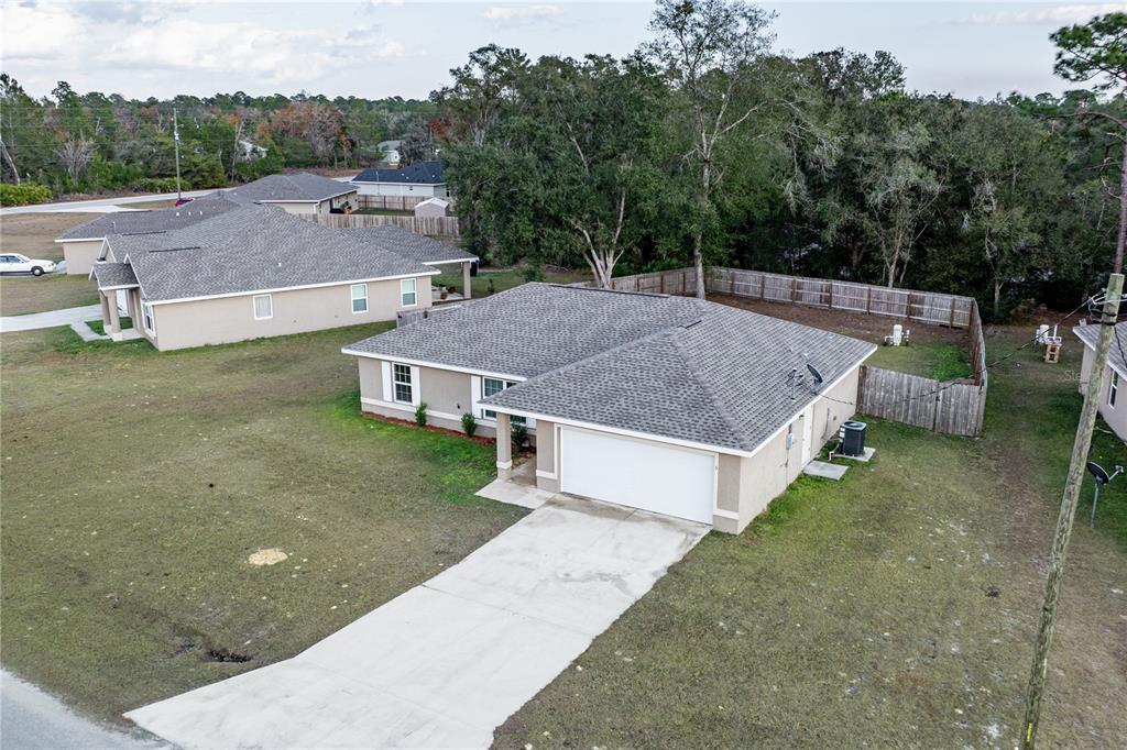 An aerial view shows a single-story house with a concrete driveway and a fenced backyard — 5 MALAUKA RADIAL CIRCLE, OCKLAWAHA, FL
