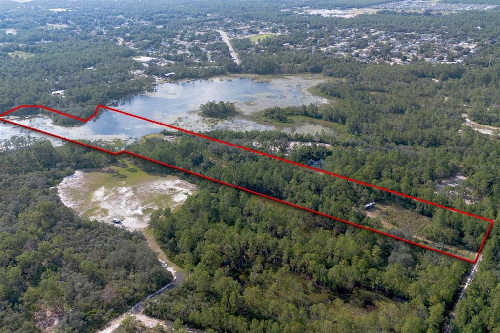 An aerial view shows a wooded lot with a lake and a red boundary line — 826 FRONTIER TRAIL, OSTEEN, FL