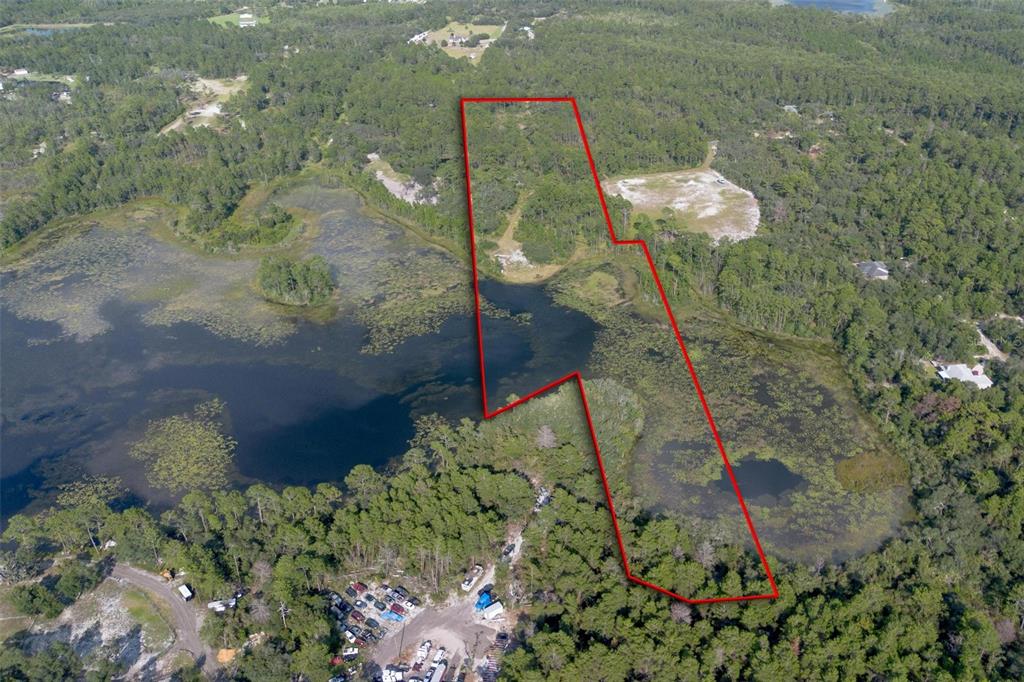 An aerial view shows a wooded plot of land with a large pond outlined in red — 826 FRONTIER TRAIL, OSTEEN, FL
