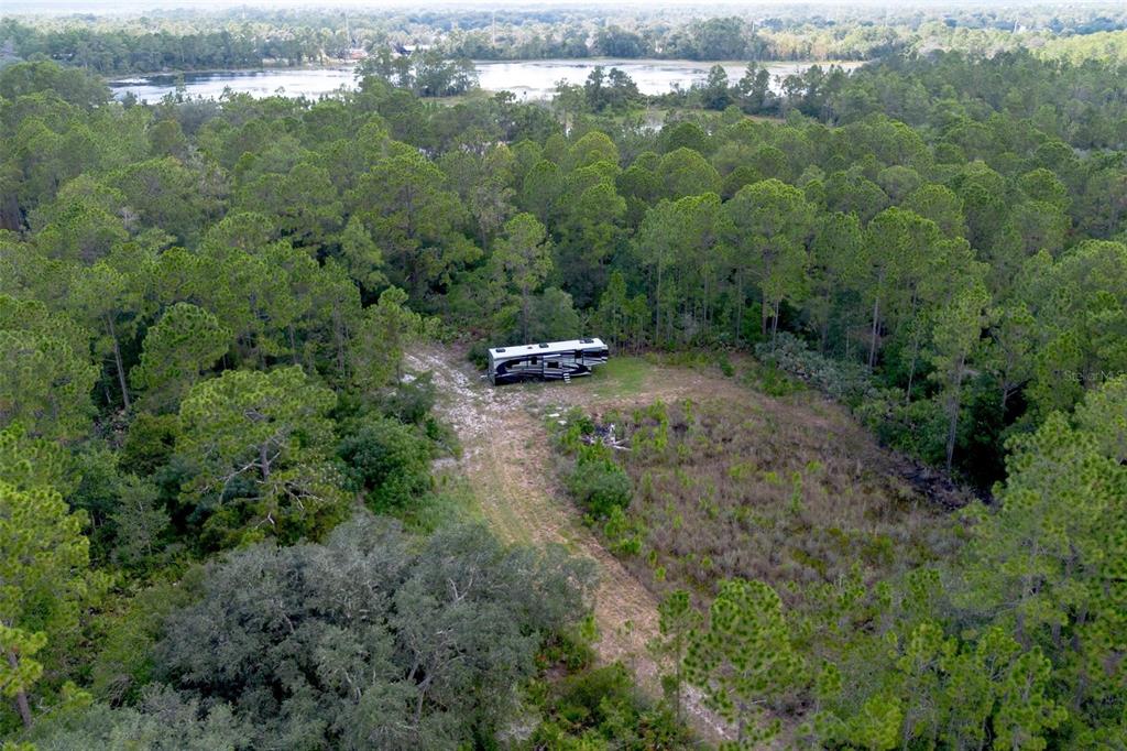 An aerial view shows a recreational vehicle parked on a dirt path in a wooded area — 826 FRONTIER TRAIL, OSTEEN, FL