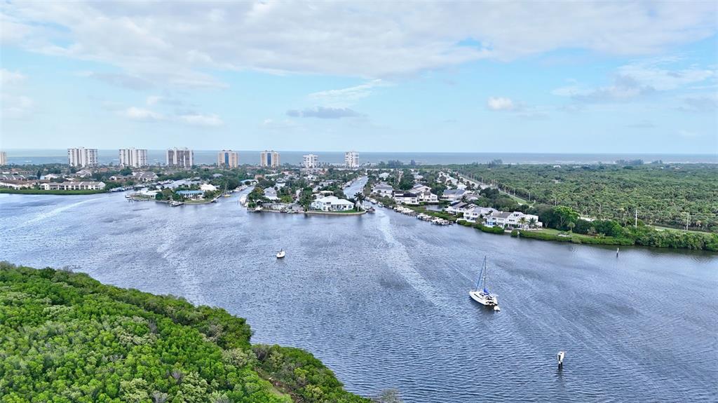 An aerial view shows a waterway winding through coastal vegetation toward high-rise buildings and ocean — 2486 HARBOUR COVE DRIVE, HUTCHINSON ISLAND, FL