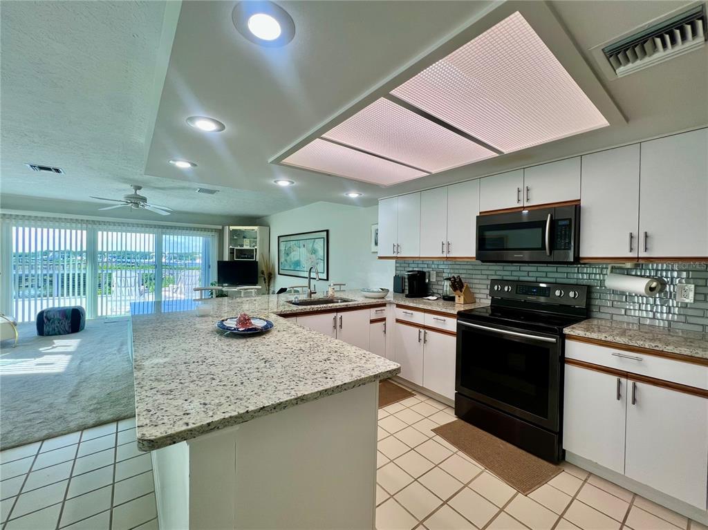 A kitchen features white cabinets, granite countertops, a black stove, and a large light fixture — 2486 HARBOUR COVE DRIVE, HUTCHINSON ISLAND, FL