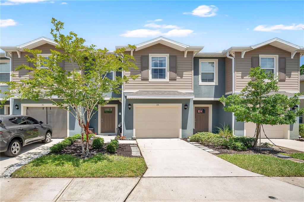 A row of three two-story townhouses with beige siding, gray stucco, and attached garages — 33 BELLA OAKS DRIVE, PORT ORANGE, FL