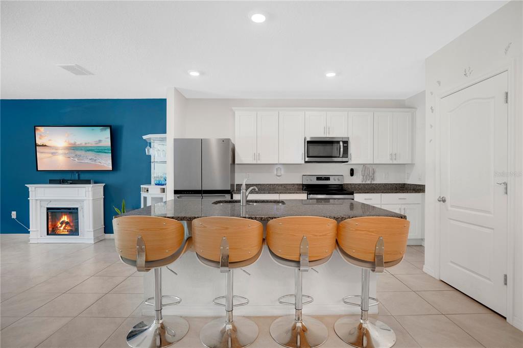 A kitchen with white cabinets, granite countertops, and four bar stools facing a blue wall — 33 BELLA OAKS DRIVE, PORT ORANGE, FL