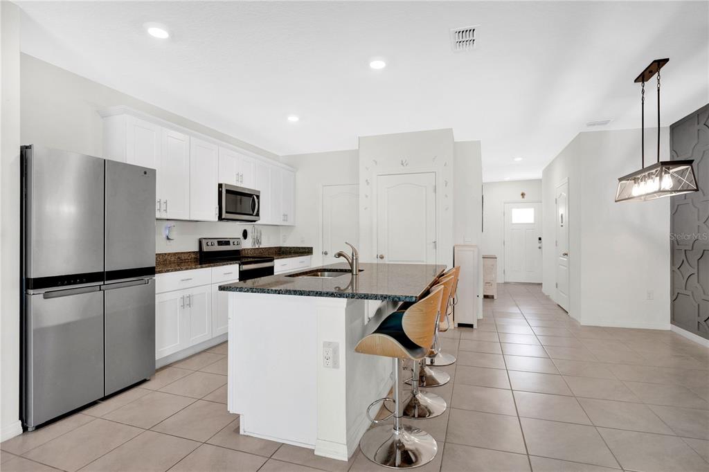A modern kitchen features white cabinets, granite countertops, a center island, and stainless steel appliances — 33 BELLA OAKS DRIVE, PORT ORANGE, FL
