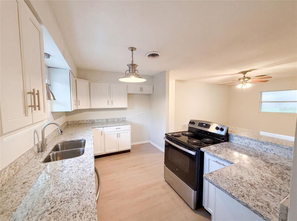 A kitchen features white cabinets, granite countertops, stainless steel appliances, and light wood-look flooring — 827 DORA AVENUE, TAVARES, FL