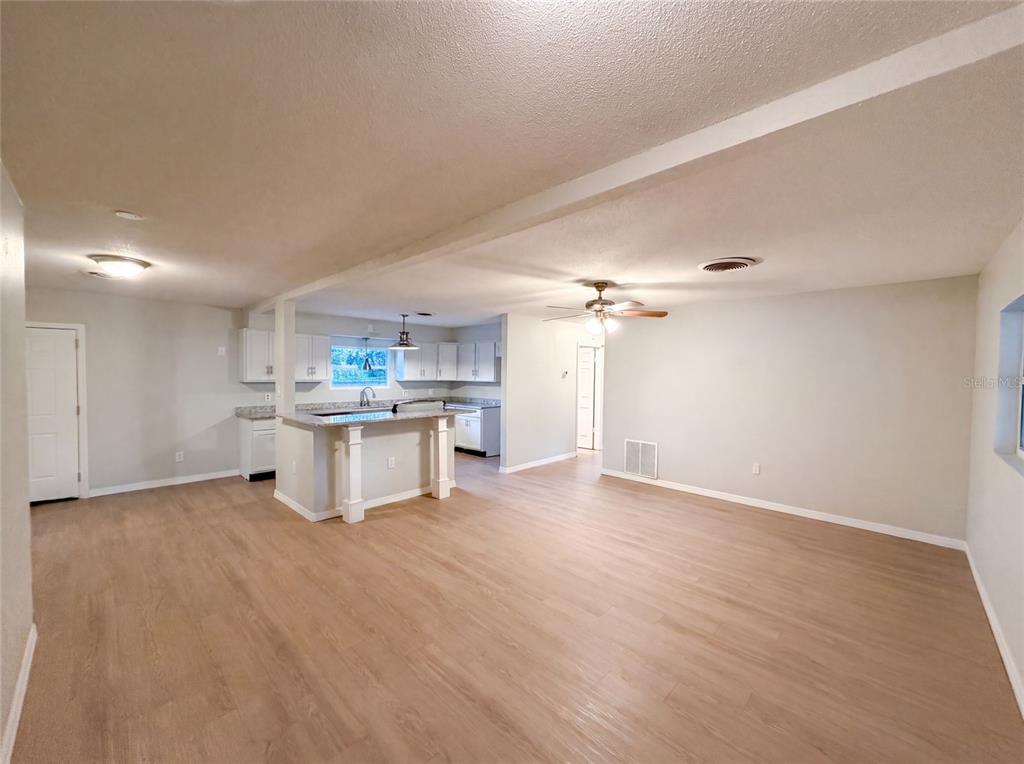 An open-concept living area features light wood-look flooring and a kitchen with white cabinets — 827 DORA AVENUE, TAVARES, FL