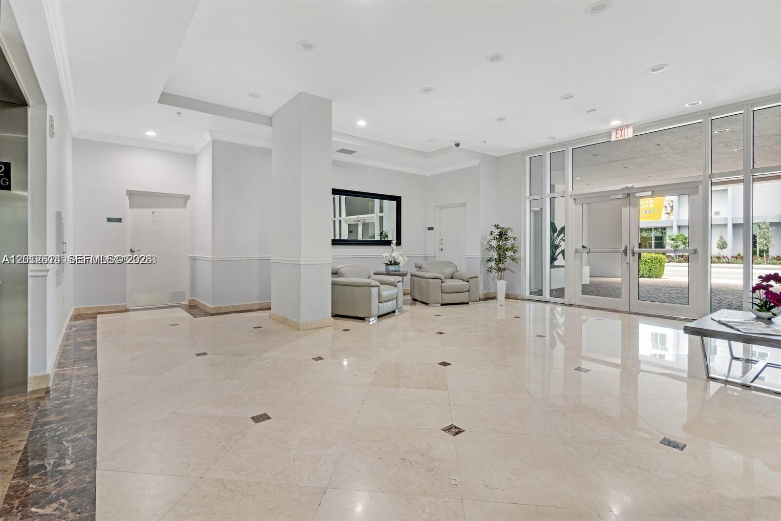 A bright lobby features light-colored tile flooring, two armchairs, and glass entrance doors — 60 NW 37th Ave # 1208, Miami FL 33125, MIAMI, FL