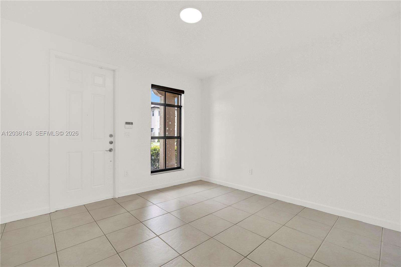 An empty room features white walls, light-colored tile flooring, a white door, and a window — 11467 SW 236th Ln, Homestead FL 33032, HOMESTEAD, FL