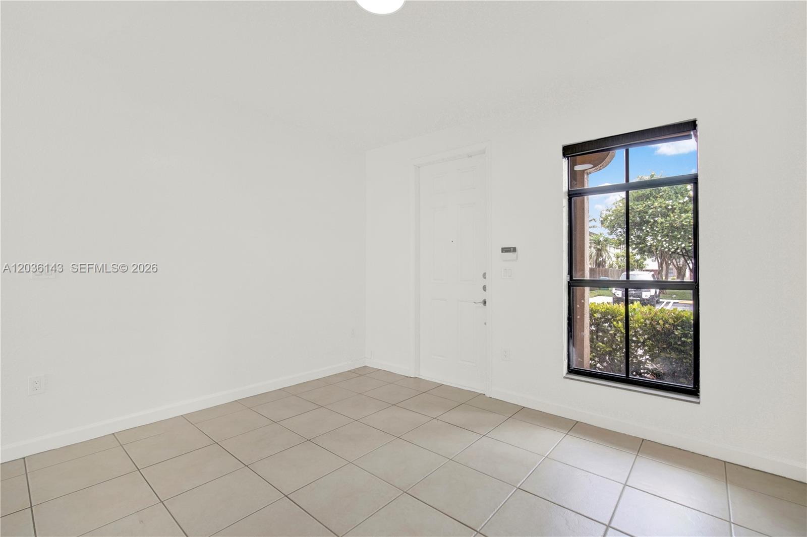 An empty room features white walls, light-colored tile flooring, a white door, and a window — 11467 SW 236th Ln, Homestead FL 33032, HOMESTEAD, FL