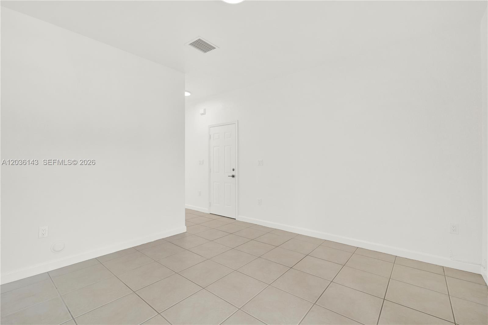 A bright, empty room features white walls, light-colored tile flooring, and a single white door — 11467 SW 236th Ln, Homestead FL 33032, HOMESTEAD, FL