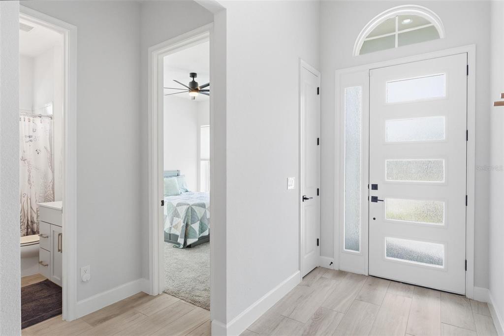 An entryway with light wood-look flooring, a white front door, and doorways to a bedroom — 270 AZURE MIST WAY, DAYTONA BEACH, FL