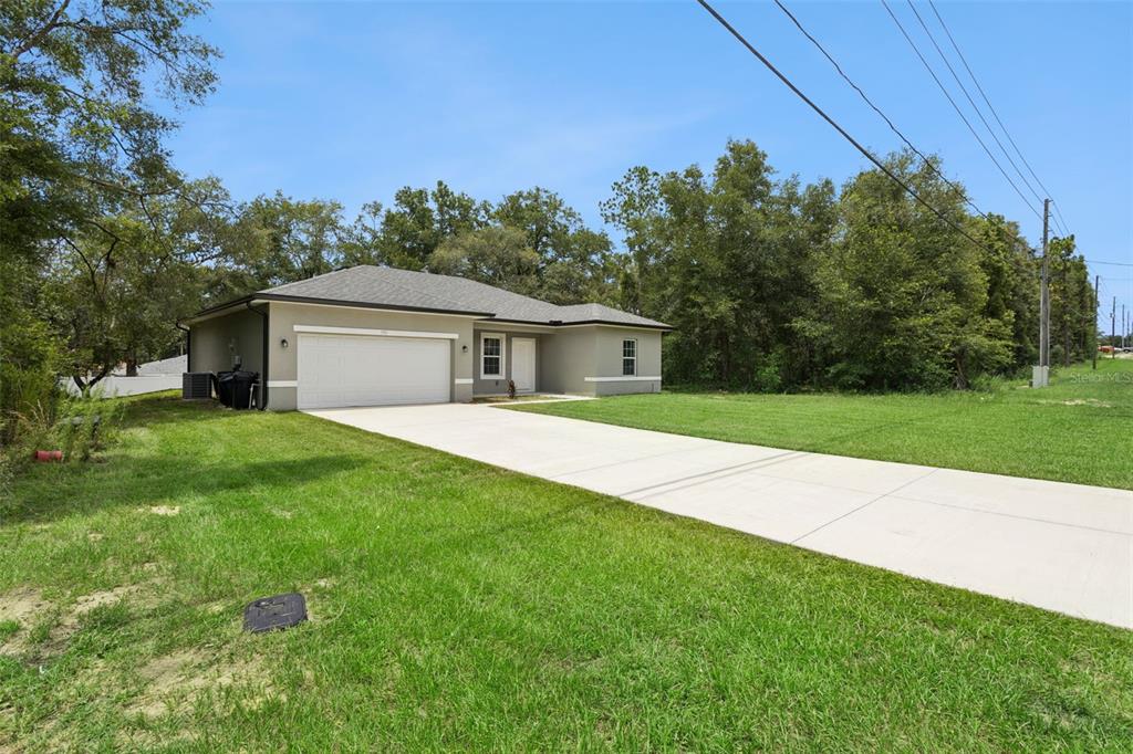 A single-story house with a white garage door and a concrete driveway sits on a lawn — 799 W COUNTRY CLUB BOULEVARD, CITRUS SPRINGS, FL