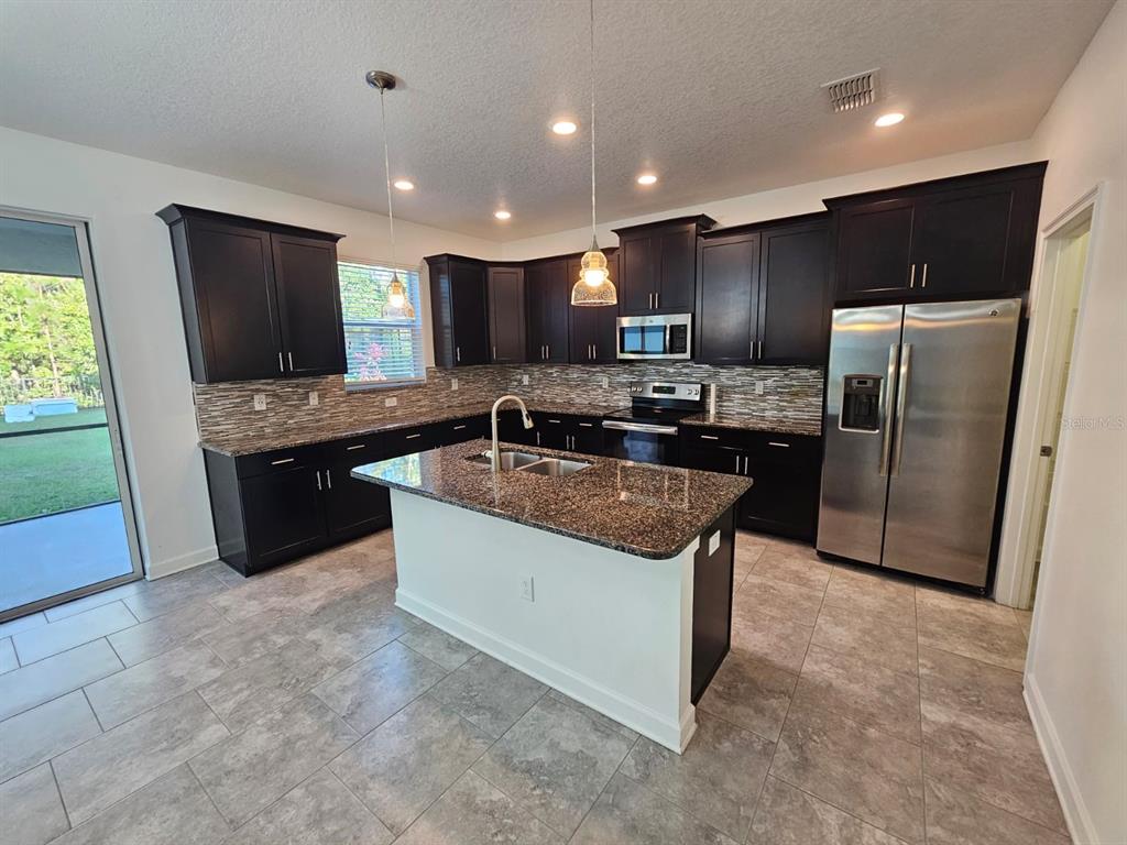 A kitchen features dark cabinetry, granite countertops, a center island, and stainless steel appliances — 3059 BEAVER CREEK DRIVE, KISSIMMEE, FL