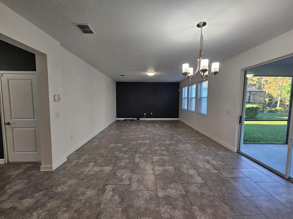 A spacious room features gray tile flooring, a dark accent wall, and a hanging chandelier — 3059 BEAVER CREEK DRIVE, KISSIMMEE, FL